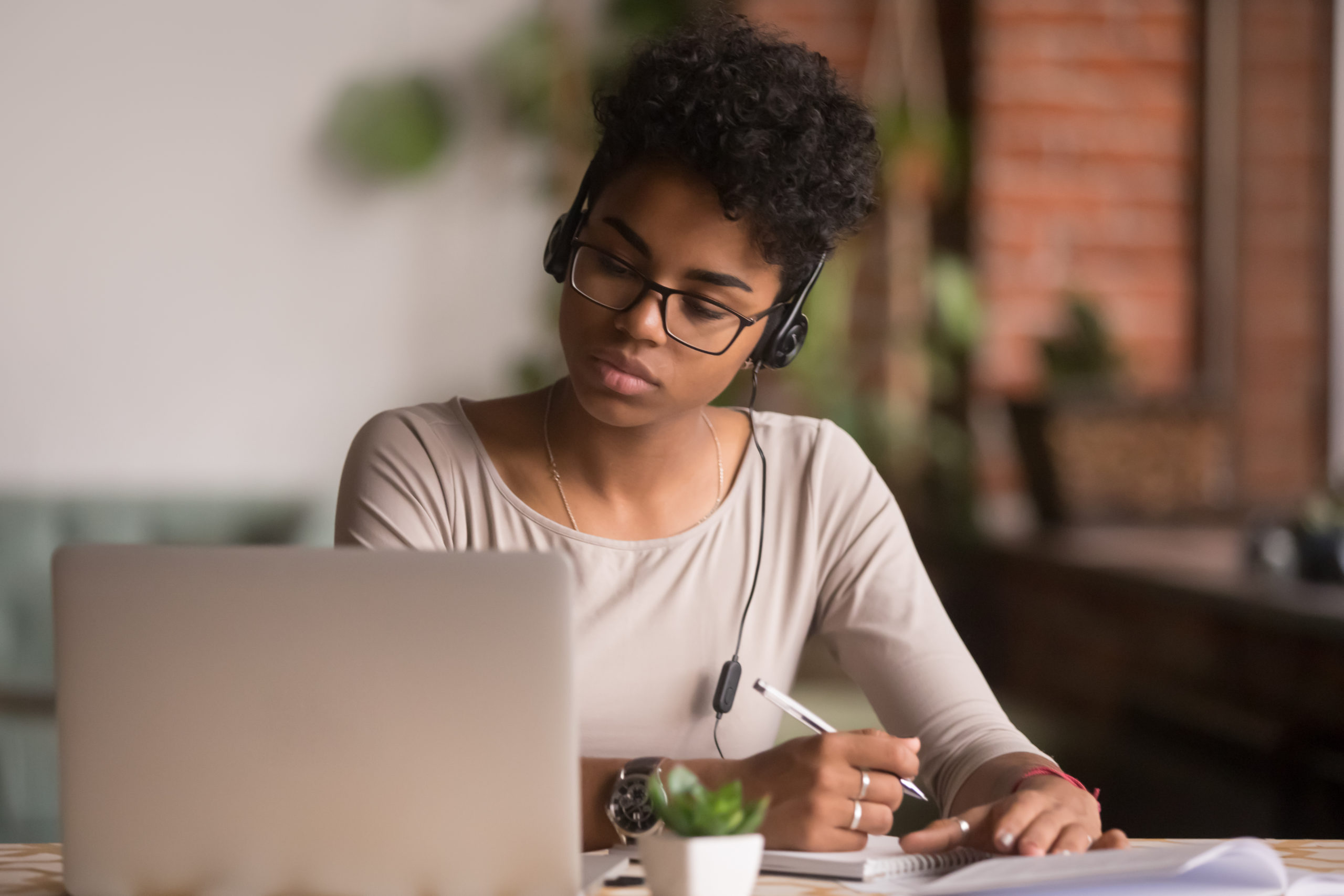 focused mixed race woman wearing headphones watching webinar write notes